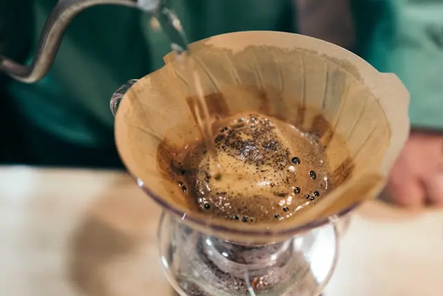 Barista pouring hot water over coffee grounds in a pour-over brewer